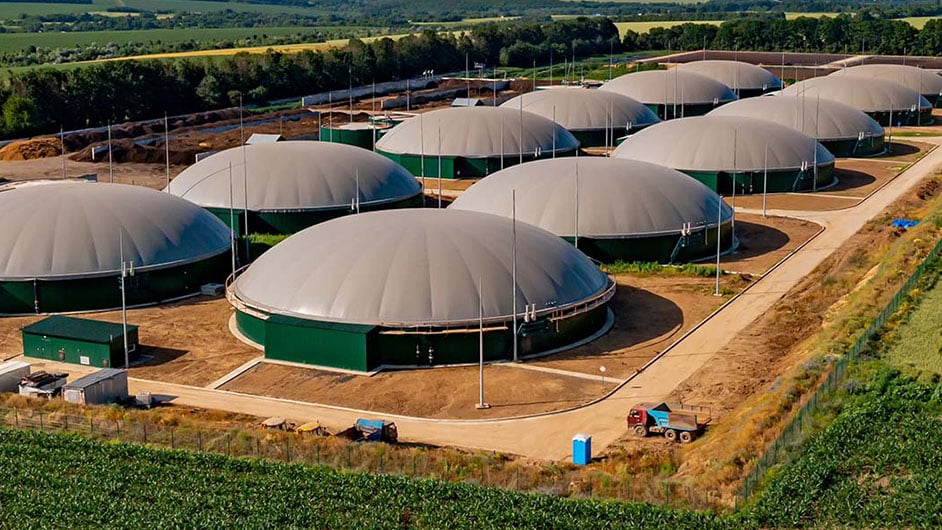 Eine Biokraftstoffanlage, die aus zwei Reihen von Kuppelbauten besteht, befindet sich inmitten einer ländlichen Anlage, umgeben von Feldern und Bäumen.