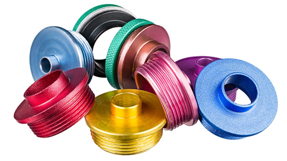 Brightly colored, round metals parts sit in a group, leaning against one another. Colors include red, light blue, yellow, pink, pink and purple metal parts.